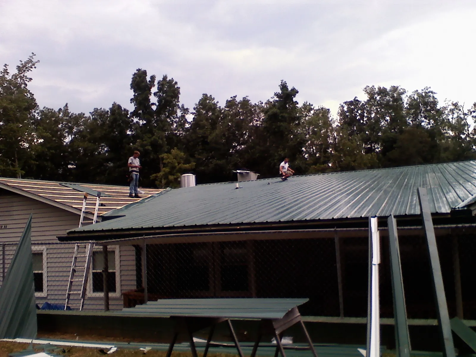 Two roofers installing green metal panels above a covered porch in Ladson