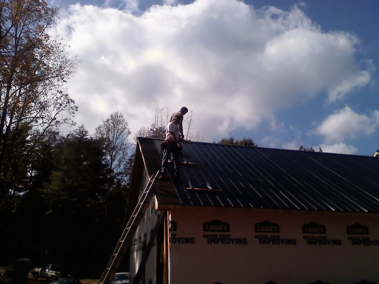 Roofer fastening dark metal panels high against a cloudy sky, from a Roof Inspection job in Ladson